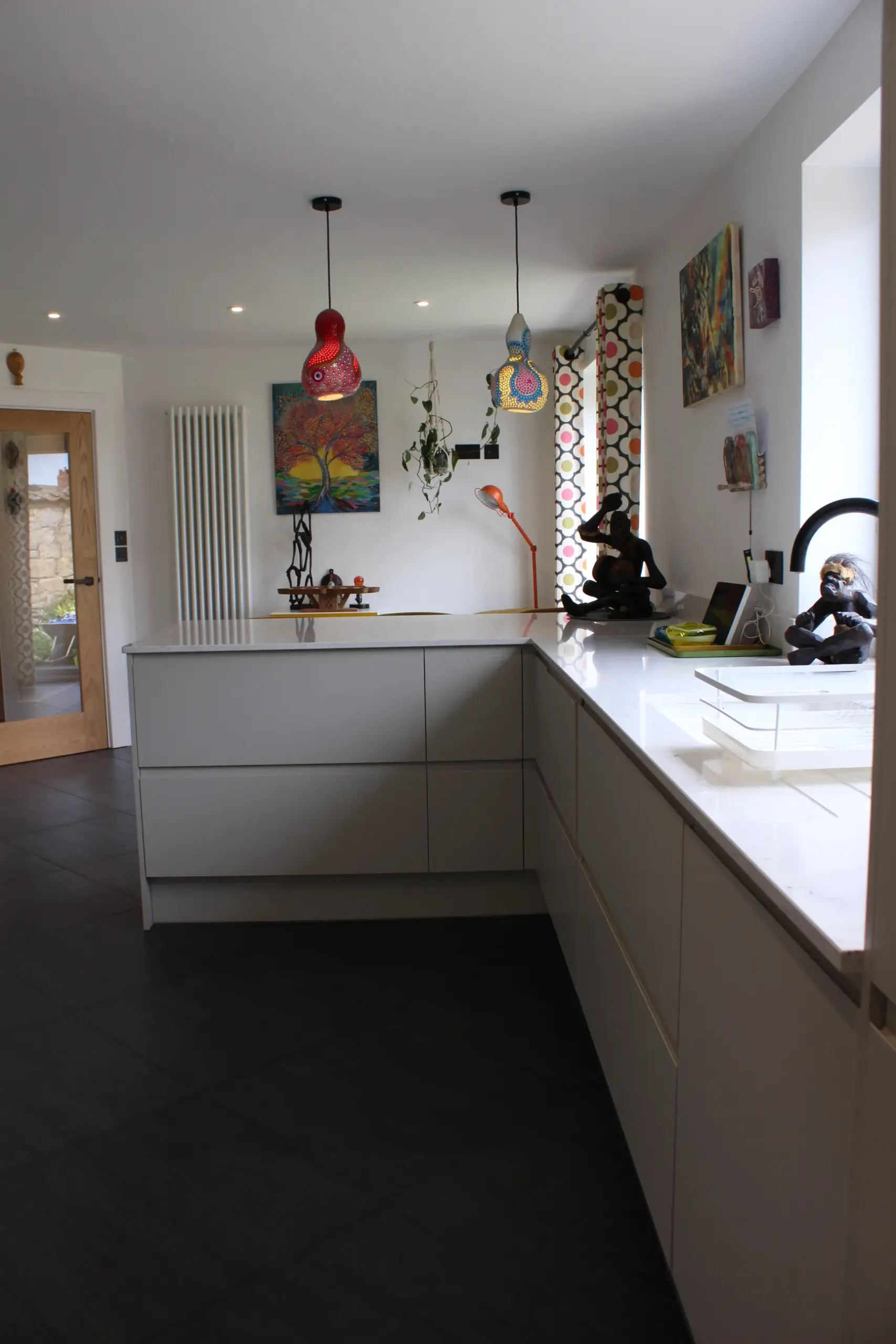 A finished open-plan space showcasing real-life rear extension kitchen ideas, featuring sleek grey handleless units, a white quartz worktop, dark flooring, and vibrant, colourful pendant lights.
